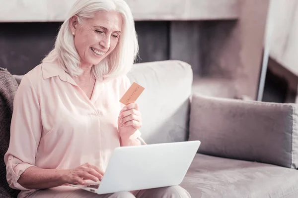Розумна старша жінка використовує ноутбук і тримає кредитну картку . — стокове фото