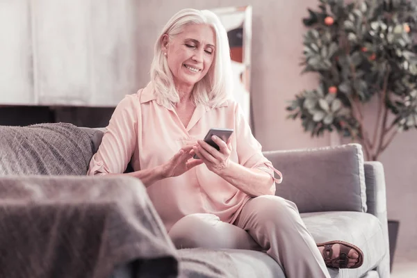 Mujer de pelo gris inteligente sentada y usando su teléfono celular . — Foto de Stock