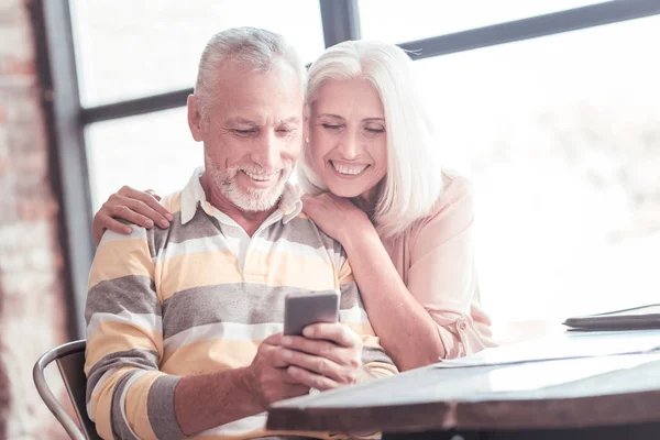 Ικανοποιημένοι χαριτωμένο ζευγάρι χαμογελώντας και κοιτάζοντας το smartphone. — Φωτογραφία Αρχείου
