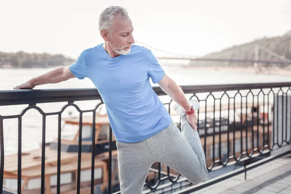 Concentrated unshaken man standing and stretching his leg. — Stock Photo, Image