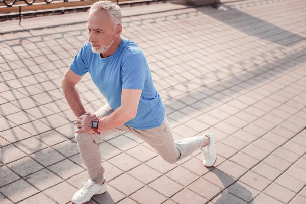 Serious aged man looking straight making stretch exercises. — Stock Photo, Image