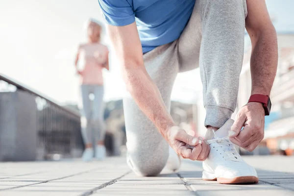 Aged attentive man standing on the knee and lacing up. — Stock Photo, Image