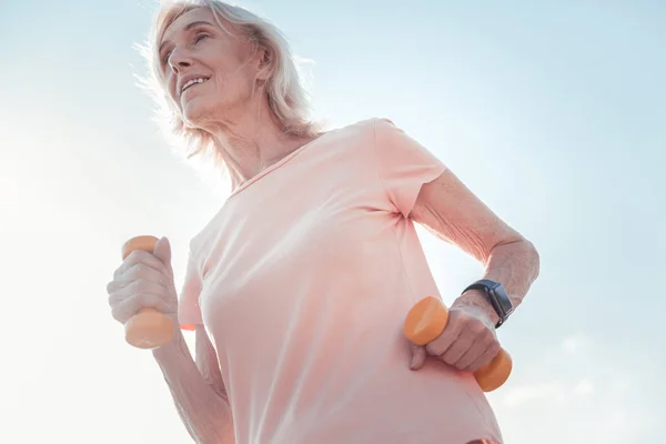 Mujer atlética satisfecha sosteniendo pesas y haciendo ejercicios de cardio . — Foto de Stock