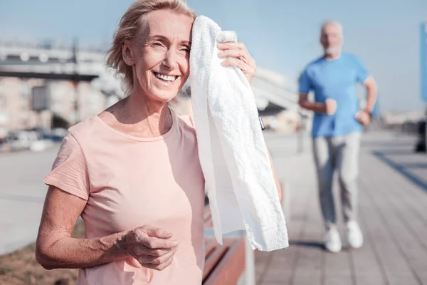 Mujer mayor satisfecha sonriendo y limpiando con una toalla . — Foto de Stock