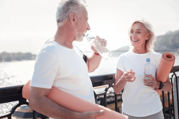 Happy senior woman standing opposite man and drinking water. — Stock Photo, Image