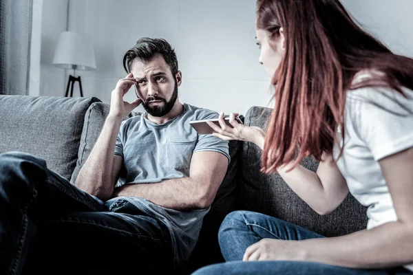 Upset beardful man sitting and holding hand near head. — Stock Photo, Image