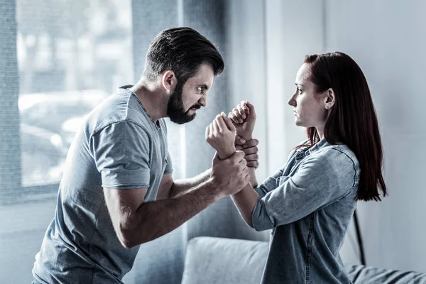 Anxious furious man holding womans hands and looking at her. — Stock Photo, Image