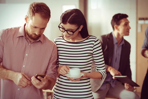 Mujer joven positiva mirando a sus colegas smartphone — Foto de Stock