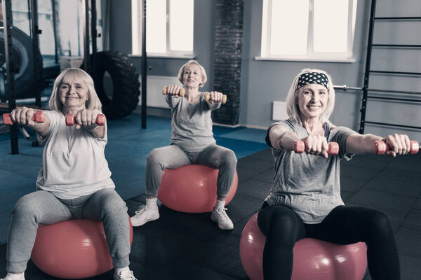 Три пожилые дамы держат гантели, сидя на мячах для упражнений

