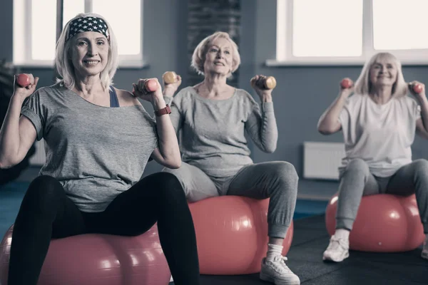 Tres mujeres animadas levantando pesas en pelotas de fitness — Foto de Stock