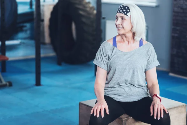 Femme rayonnante assise sur la boîte tout en se reposant dans la salle de gym — Photo