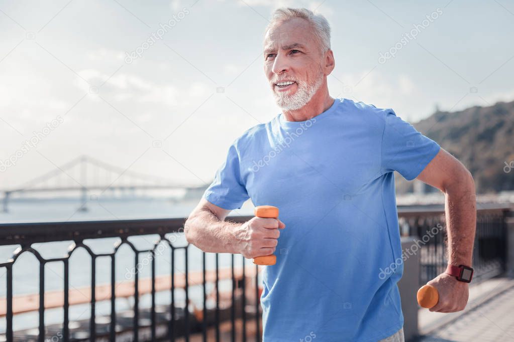 Confident senior man holding dumbbells and running.