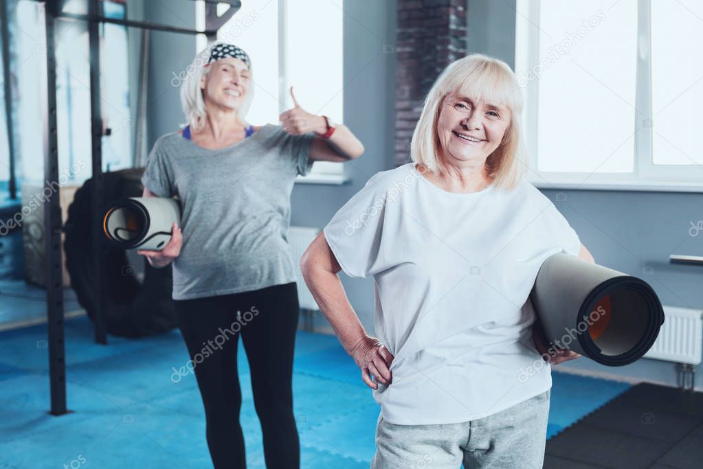 Kind smiling lady holding mat while taking group exercise class