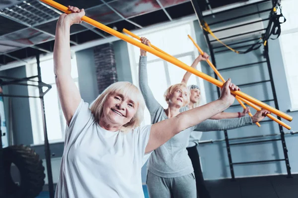 Mujeres alegres con palo haciendo ejercicio de flexión lateral en el gimnasio —  Fotos de Stock