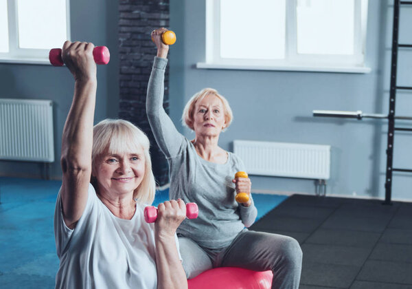 Two elderly ladies lifting weights while training in gym