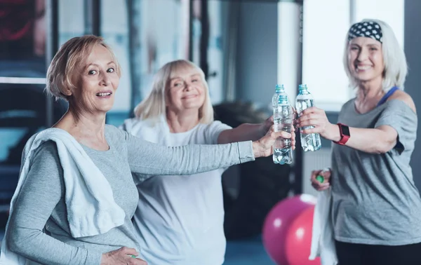 Positive minded retired friends joining bottle of water after training — Stock Photo, Image