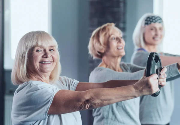 Excited senior lady holding weight disk while training