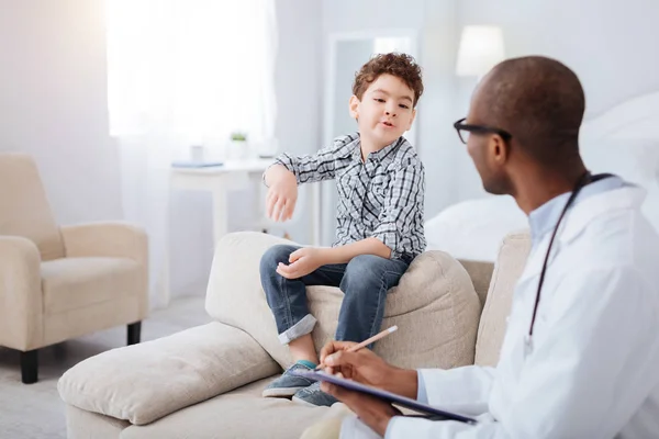 Serious boy explaining his state to male doctor — Stock Photo, Image