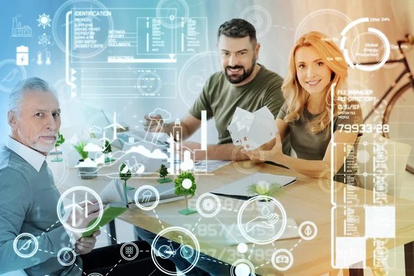 Smiling woman holding a miniature house while sitting with coworkers — Stock Photo, Image