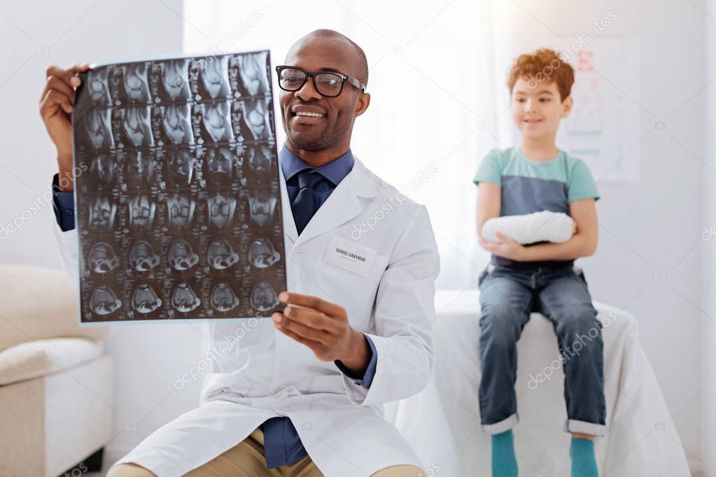 Pleasant male doctor examining boys radiograph