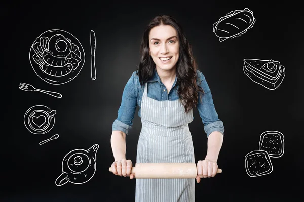 Känslomässiga kvinna leende medan du håller en brödkavel och matlagning — Stockfoto