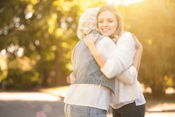 Positive young woman hugging pensioner outdoors — Stock Photo, Image
