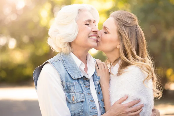Mujer involucrada besando a madre anciana en el parque —  Fotos de Stock