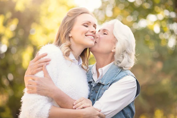 Åldrande mor kyssar kärleksfull dotter i parken — Stockfoto