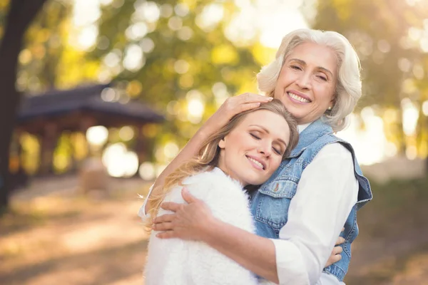 Retired mother hugging lively daughter in the park — Stock Photo, Image