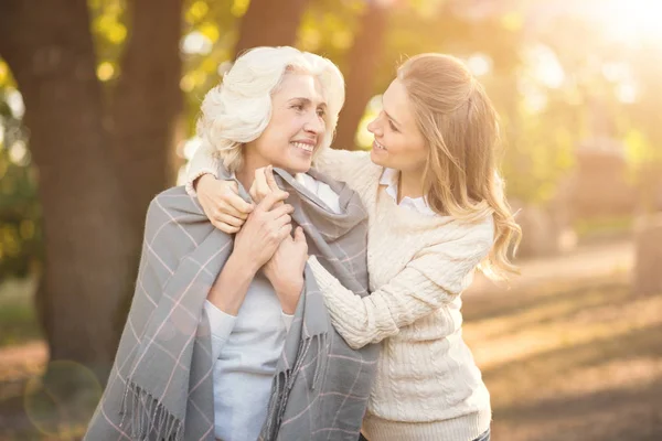 Loving young woman covering old mother with blanket outdoors — Stock Photo, Image