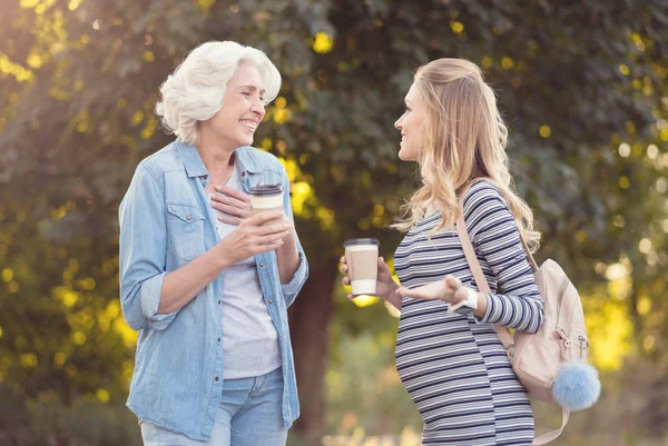 Amused pregnant woman enjoying conversation with retired mother outdoors — Stock Photo, Image