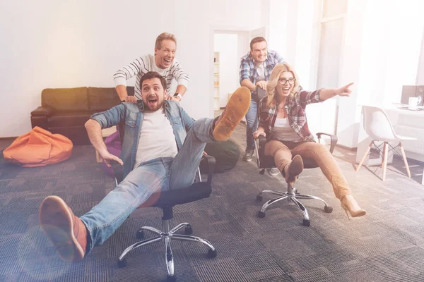 Positive smiling colleagues riding in office chairs — Stock Photo, Image