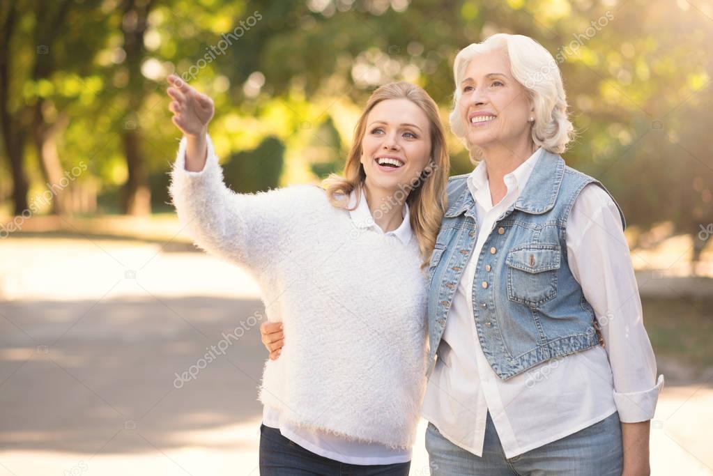 Happy aging woman and mature daughter walking in the park