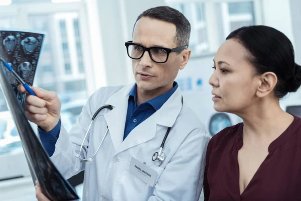 Médico concentrado mostrando un escáner cerebral también su paciente — Foto de Stock