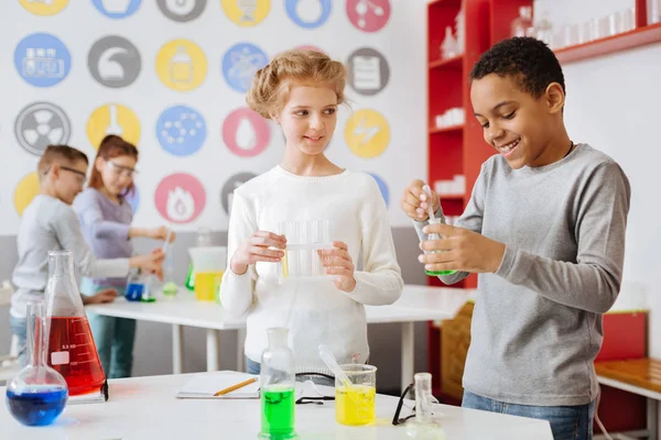 Menino alegre adicionando produto químico ao frasco durante a aula de química — Fotografia de Stock