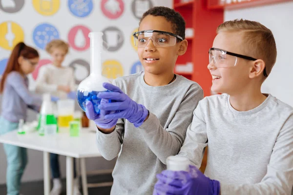 Pleasant students watching blue substance reacting in flask — Stock Photo, Image