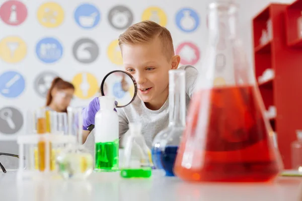 Estudante alegre usando lupa para estudar a reação química — Fotografia de Stock