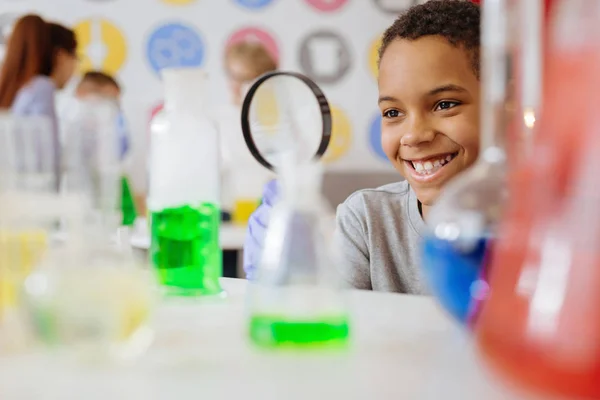 Школярка, посміхаючись, перевіряє вміст хімічної колби — стокове фото