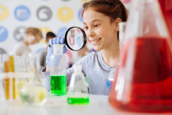 Chica alegre examinando el resultado de la reacción química con lupa — Foto de Stock
