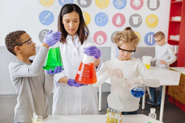 Νεαρή δασκάλα ελέγχει τα αποτελέσματα της χημικής πειραμάτων οι μαθητές — Φωτογραφία Αρχείου