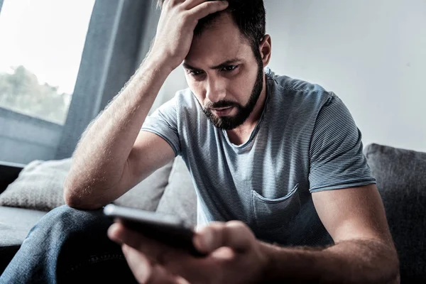 Нещасний безвеселий чоловік дивиться на екран свого смартфона — стокове фото