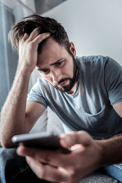 Грустный депрессивный мужчина держит свой смартфон
