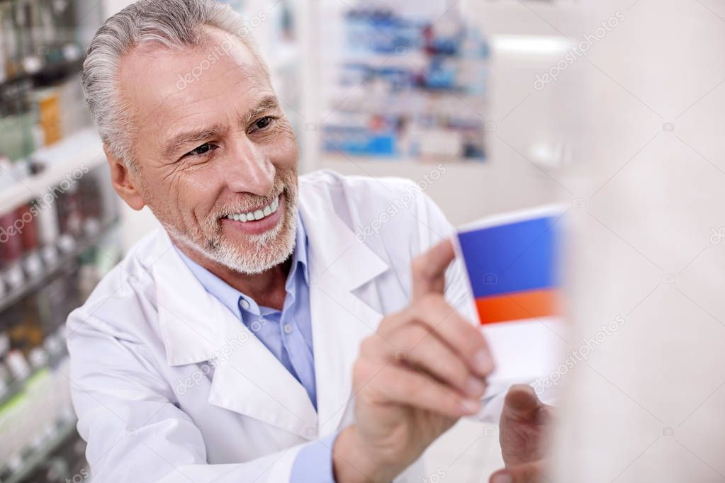 Joyful male pharmacist putting drug on shelf