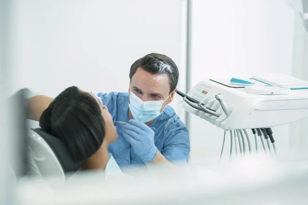 Концентрированный стоматолог-мужчина осматривает зубы своих пациентов — стоковое фото