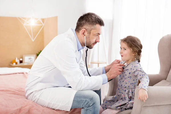 Skoncentrowany lekarz słucha bicia serca dziewczyny — Zdjęcie stockowe