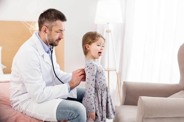 Médico general concentrado escuchando los latidos del corazón de las chicas — Foto de Stock