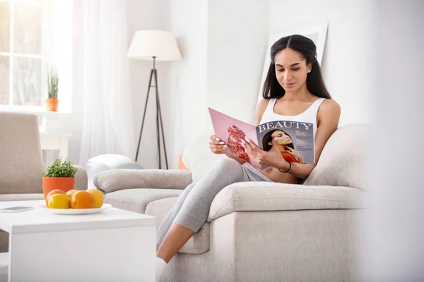Slim young woman learning beauty tricks from magazine — Stock Photo, Image