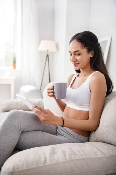 Mujer delgada alegre usando tableta y bebiendo té —  Fotos de Stock