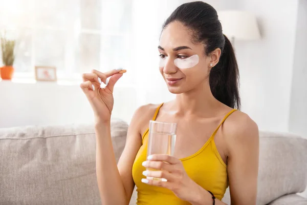 Mujer joven agradable con parches bajo los ojos que toman la píldora de la vitamina —  Fotos de Stock