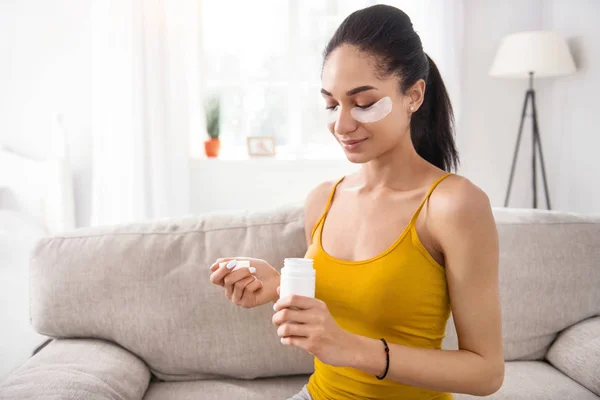 Pleasant young woman looking inside bottle of vitamins